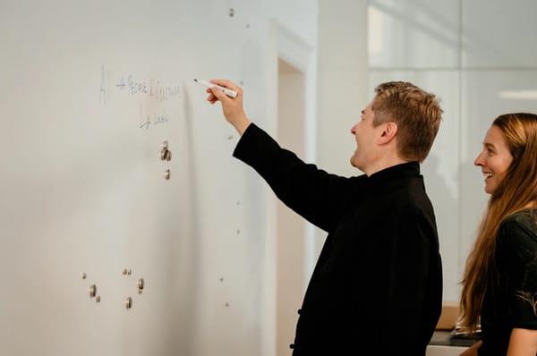 Kollega skriver AI → People & Culture på en tavle, mens en anden ser til