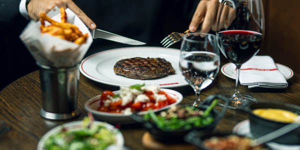 Restaurantbord med steak, pommes frites og et glas rødvin