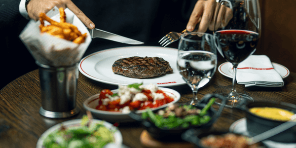 Restaurantbord med steak, pommes frites og et glas rødvin